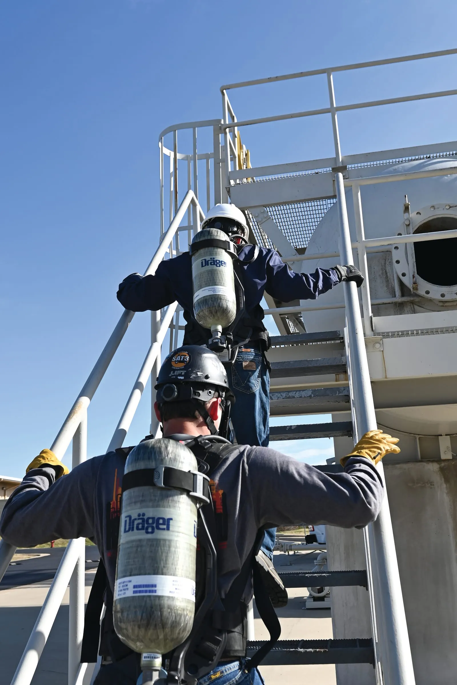 Técnicos con equipos de respiración autónoma Dräger subiendo una escalera industrial